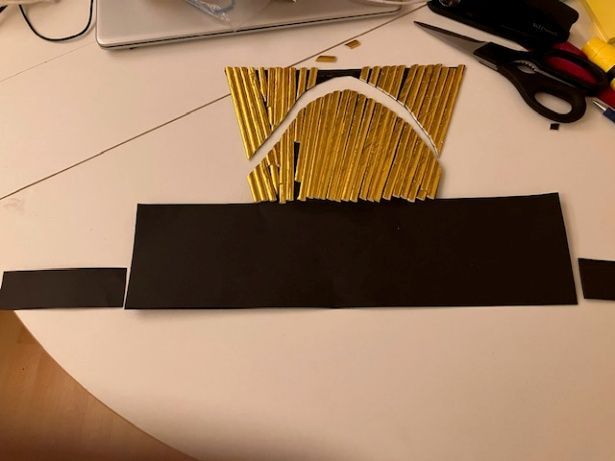 Black paper craft with yellow sticks and a white arch, resting on a desk with scissors nearby