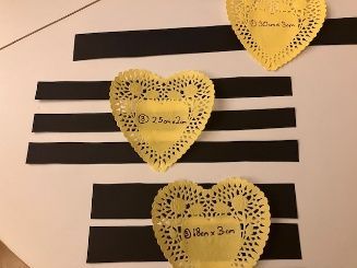 Yellow paper hearts on black horizontal strips, with one heart showing a handwritten note.