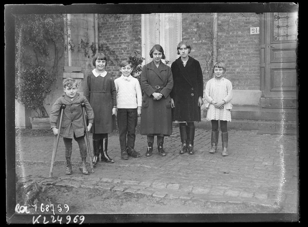 Five children standing outdoors in front of a brick building, one holding a bicycle.