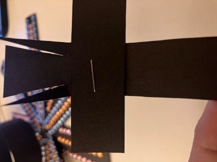 Black paper cross cutout held up against a beige background, with a hand visible on the right.