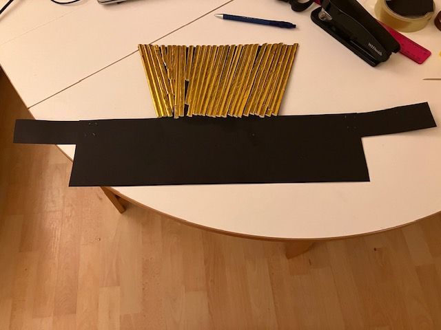 Black paper strip on a table with a yellow pencil bundle, scissors, and a black tool nearby
