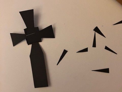 Black paper cutout figure on a light background, with several small black triangular pieces scattered nearby