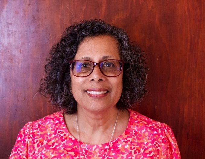 Smiling woman with glasses in a pink floral top against a wooden background