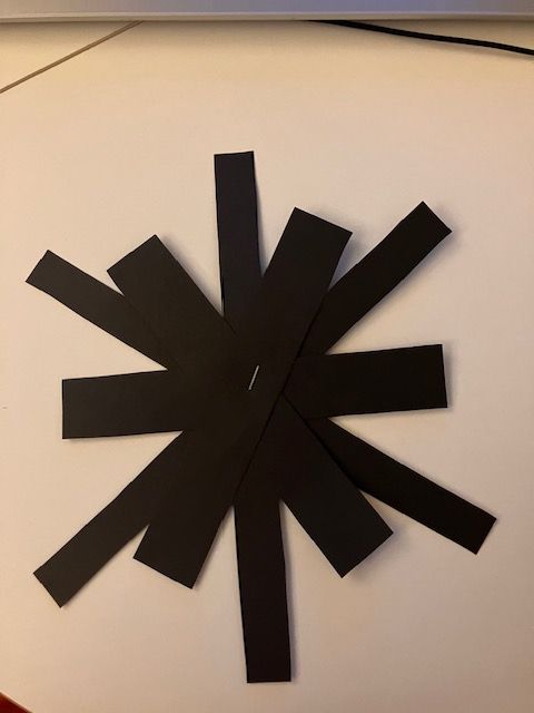Black tape strips forming an asterisk-like star on a white surface, with a red edge at right