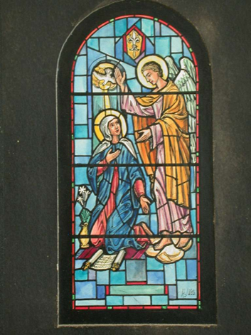 Stained glass window of angel and Mary, annunciation scene. Angel in gold, Mary in blue, dove above.