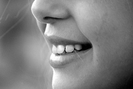 Close-up of a person's smiling mouth, teeth visible, in black and white.
