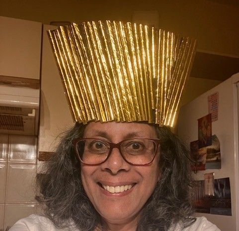 Smiling person wearing glasses and a gold paper crown indoors