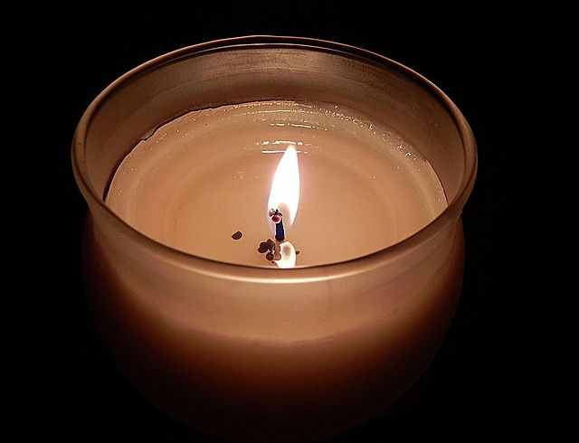 Lit candle in a glass jar, warm light against a dark background.