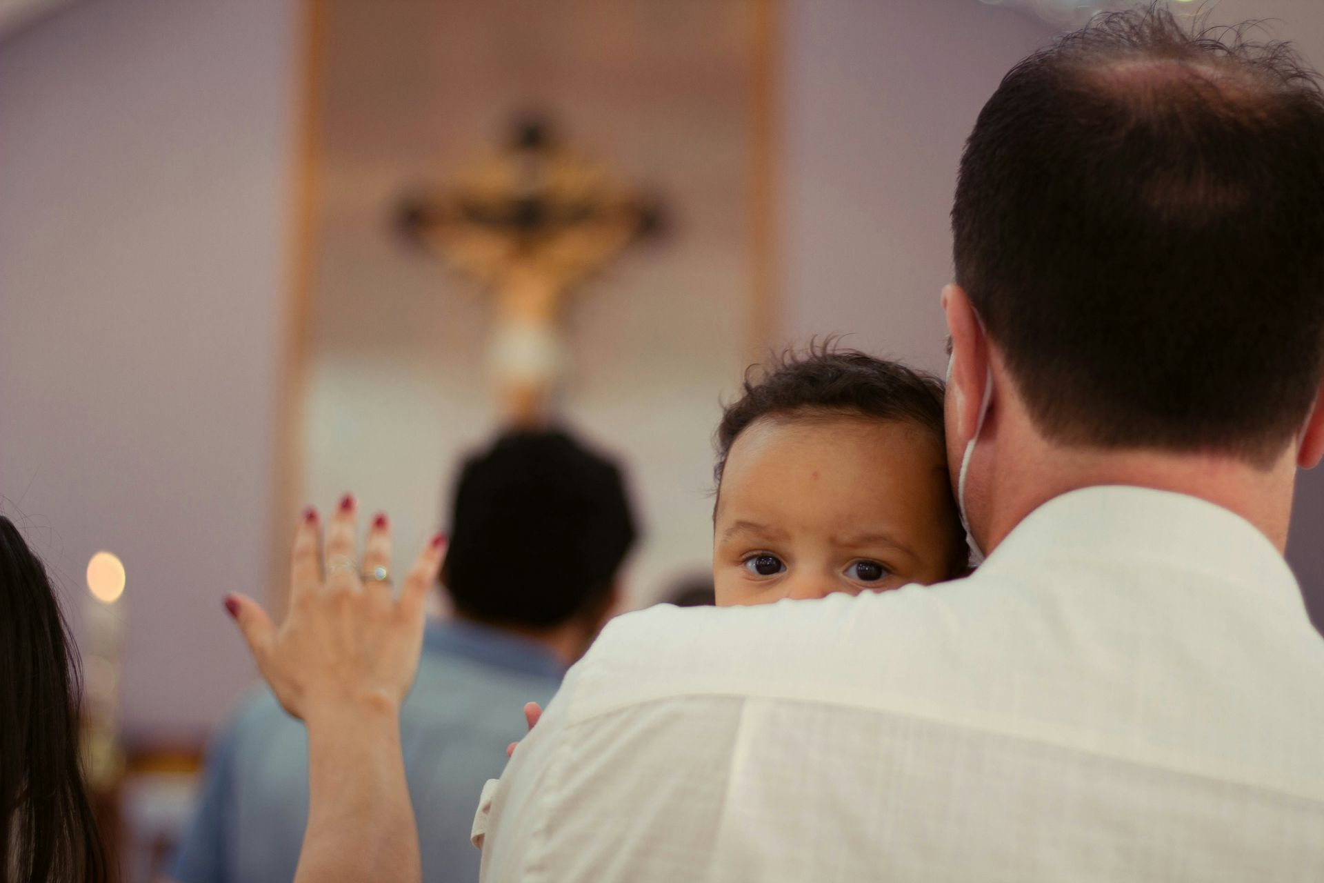 A person holds an infant over their shoulder during a church service with a crucifix in the background.