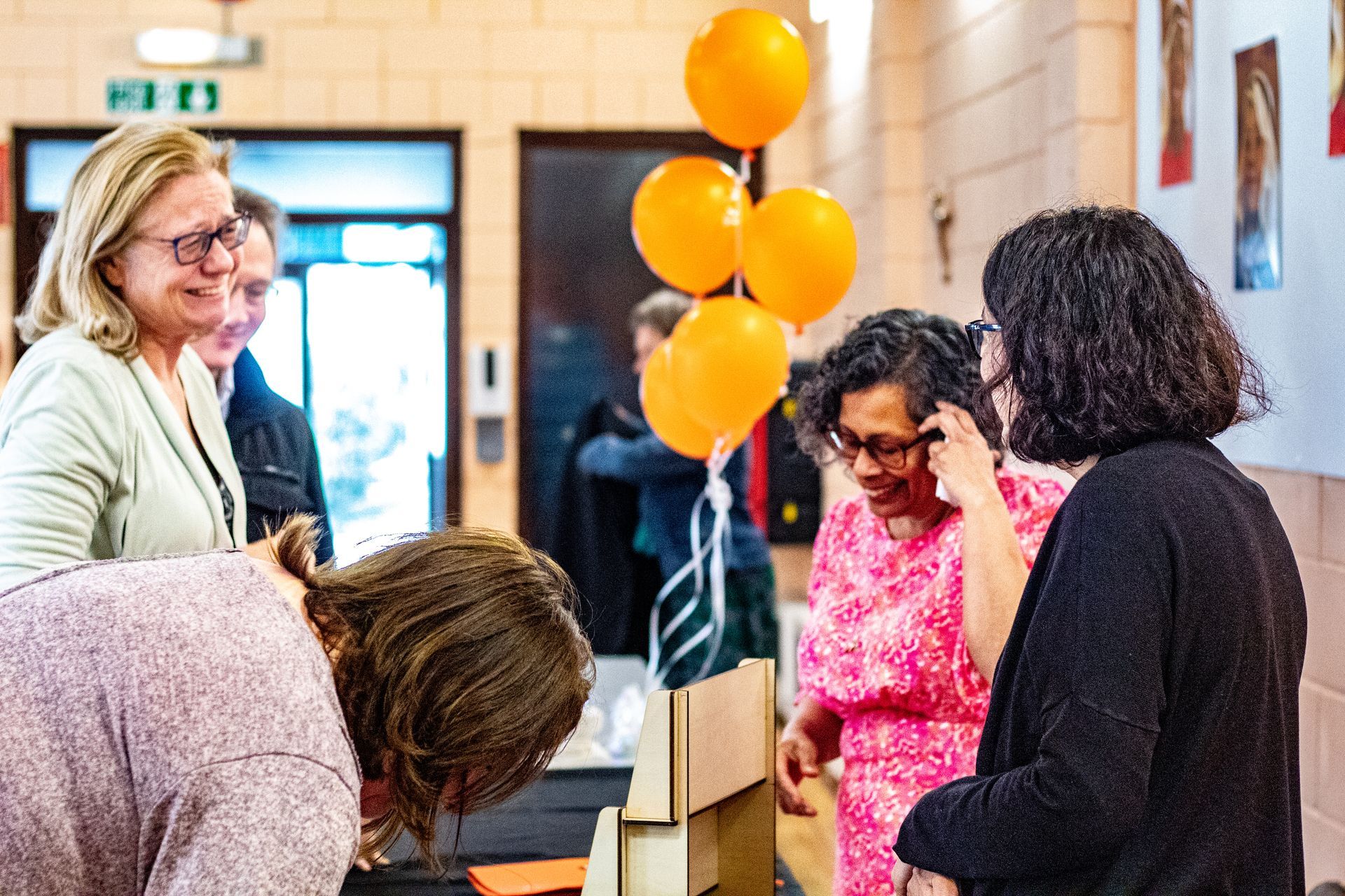 A group of people are standing around a table with balloons hanging from the ceiling.