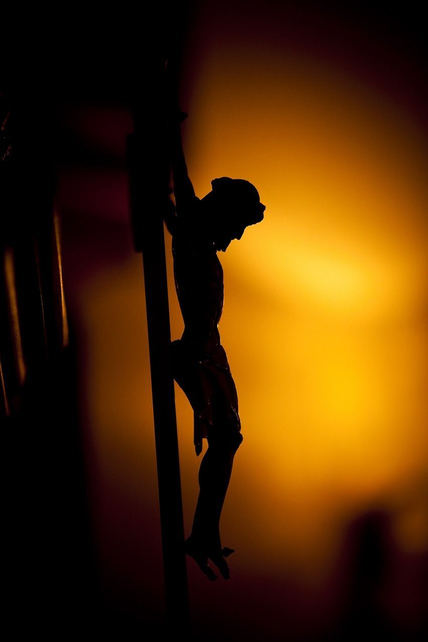 A silhouette of jesus on the cross with a yellow background