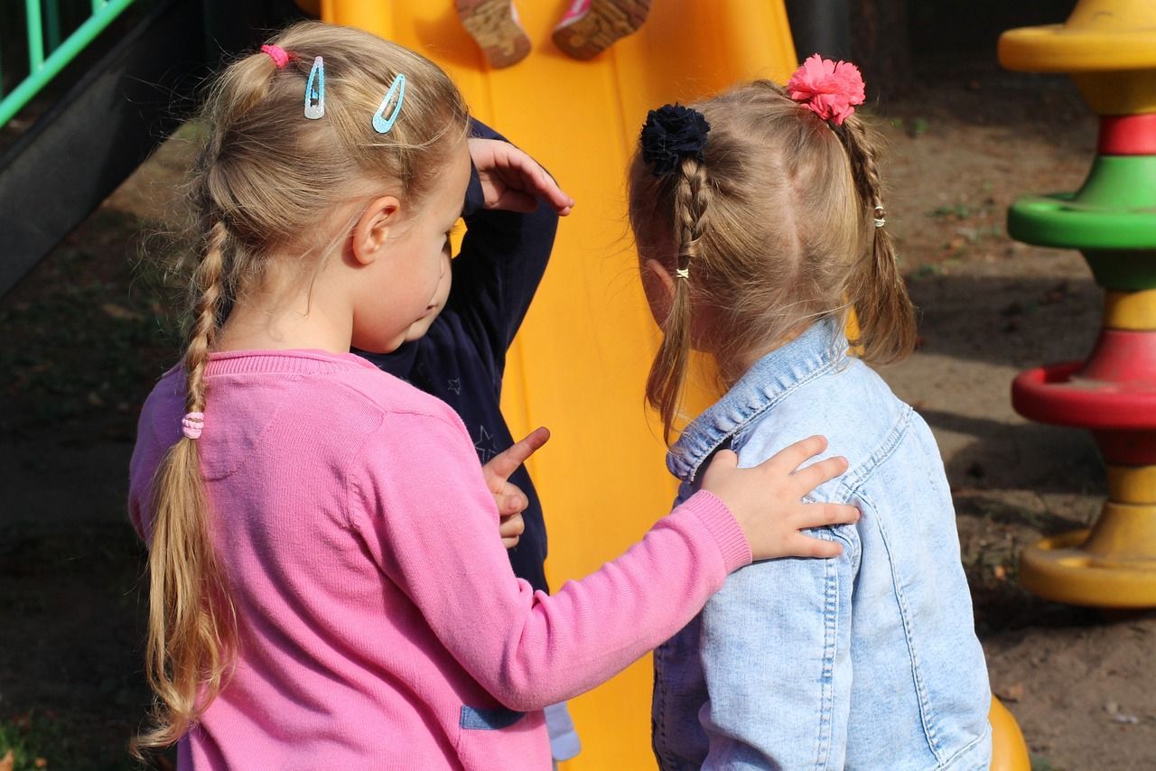 Two little girls are standing next to each other at a playground.