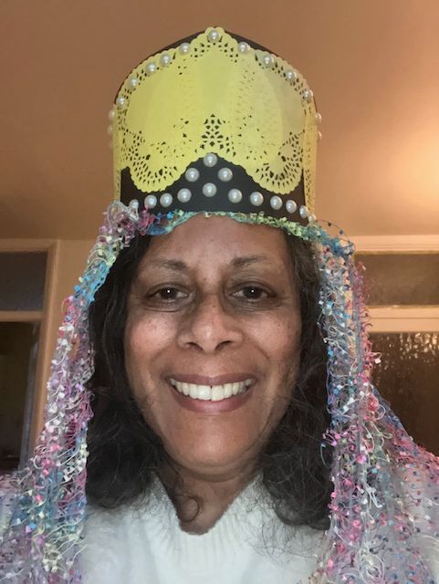 Smiling person wearing a yellow and black sequined crown with iridescent tinsel around the face