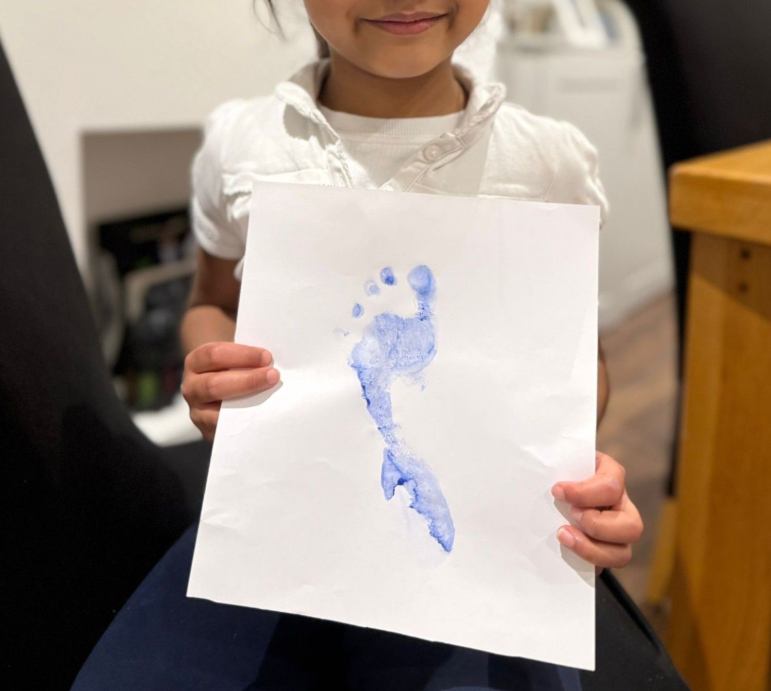 Girl holding a blue footprint art on white paper.