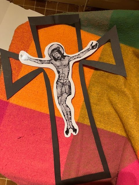 A paper cross with a Christ figure cutout, set on a colorful patterned blanket.
