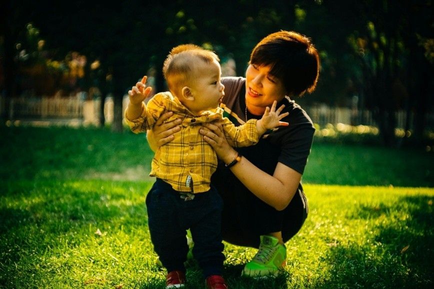 A woman is kneeling down holding a baby in her arms in a park.