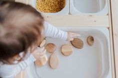A baby is playing with wooden rocks in a sink.