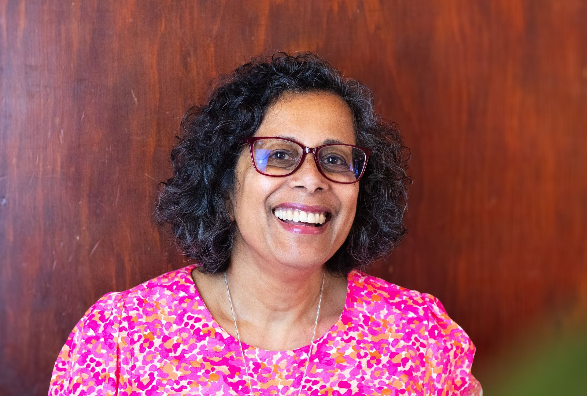 A woman wearing glasses and a pink shirt is smiling for the camera.