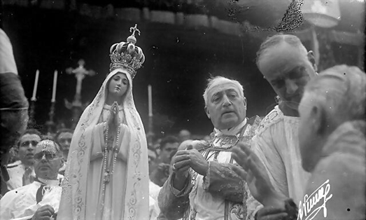Black-and-white scene of a religious procession with a crowned statue and men carrying candles outdoors