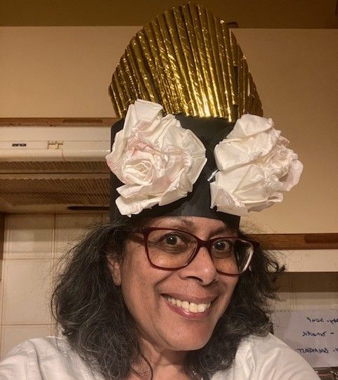 Smiling person wearing glasses and a gold-and-white paper hat indoors