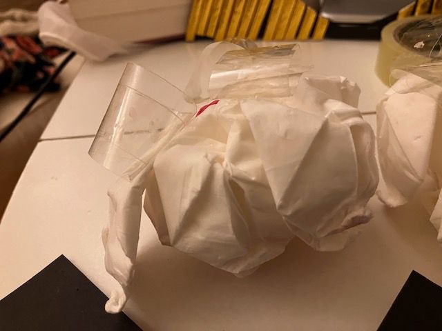 White tissue-paper bundle tied with clear tape on a table, with black paper corners and a yellow object in back.