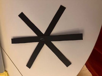Black asterisk-like symbol made of tape on a light-colored wall, near a red surface
