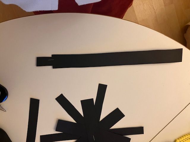 Black paper strips arranged like a spiky starburst on a white table, with a long strip above.