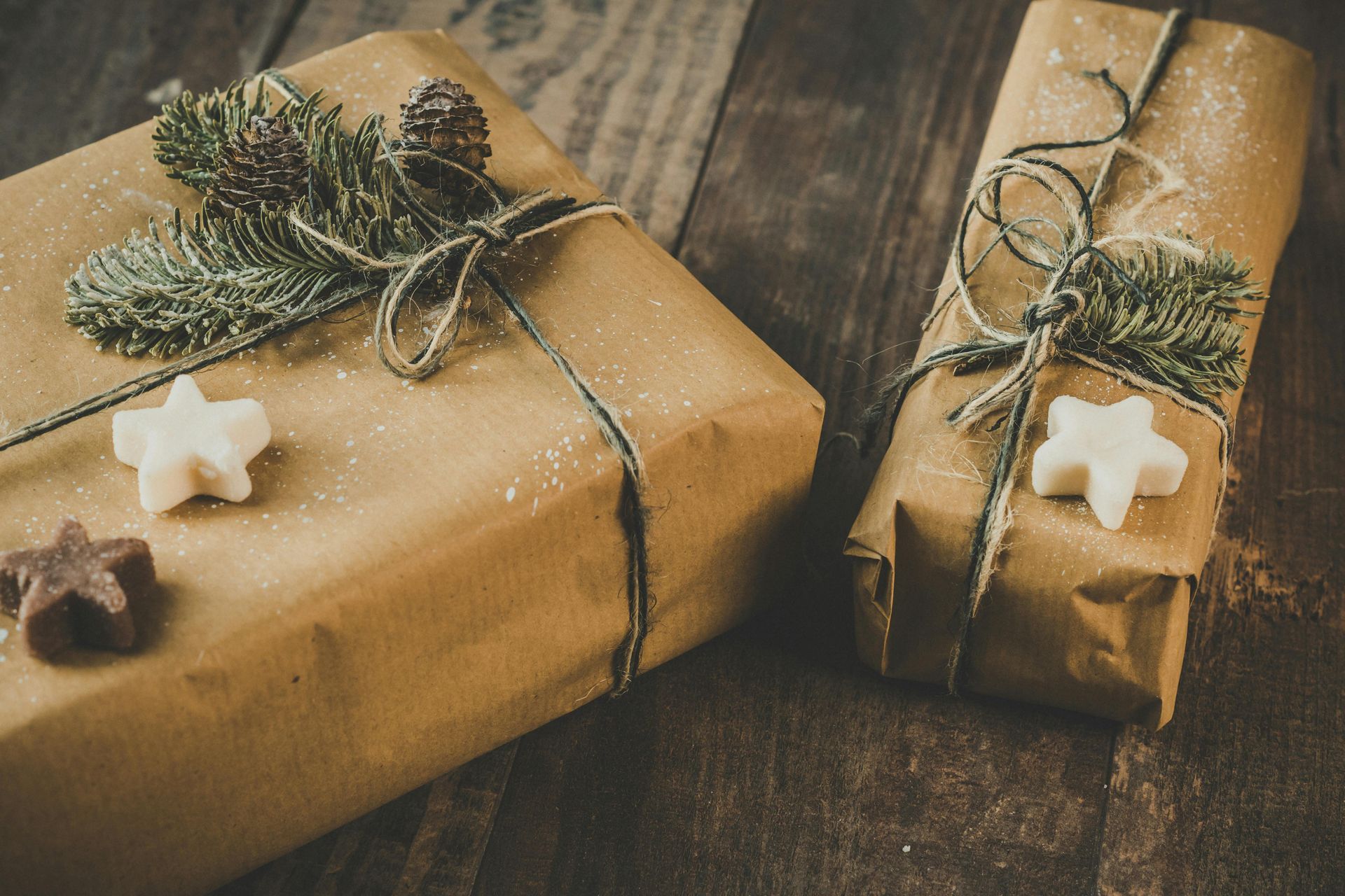 Two christmas presents wrapped in brown paper are sitting on a wooden table.