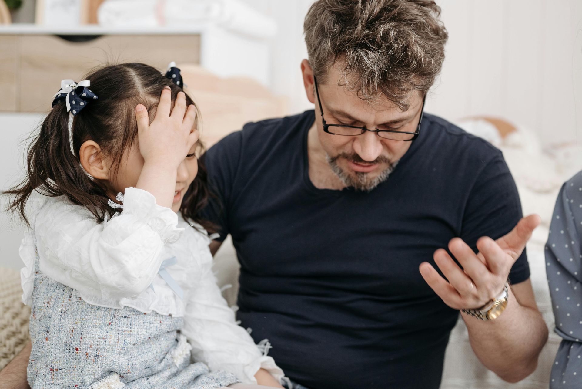 A man and a little girl are sitting on a couch . the little girl is covering her face with her hand.