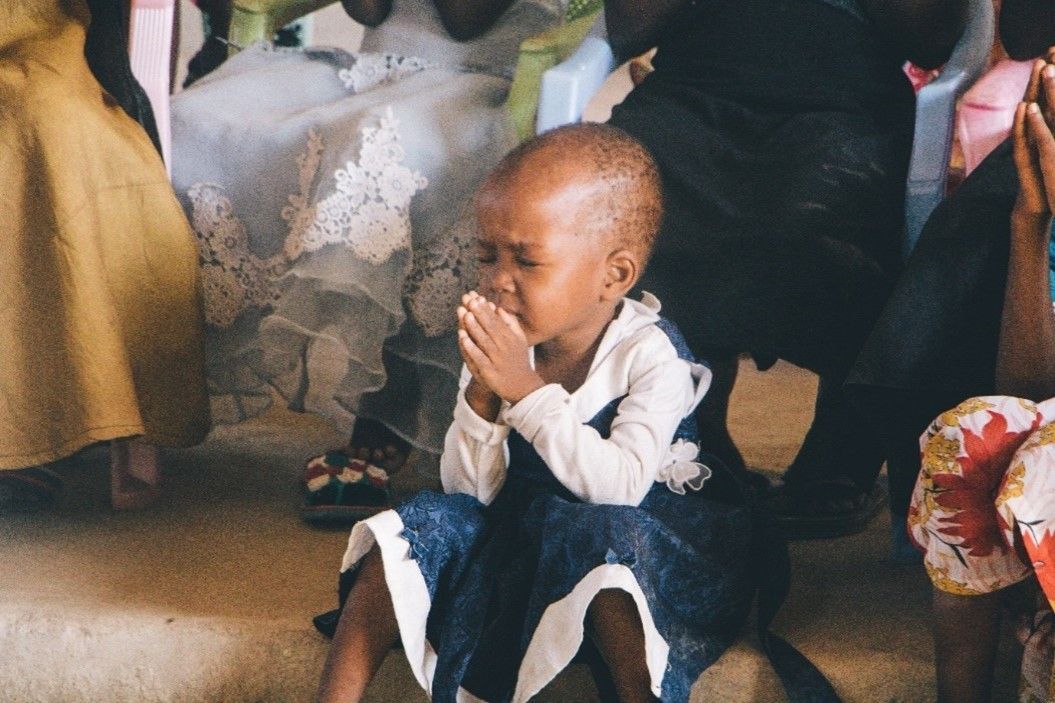 A little girl is sitting on the floor with her hands folded in prayer.