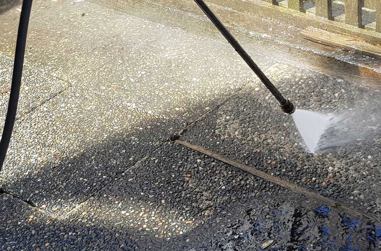 A person is using a high pressure washer to clean a sidewalk.