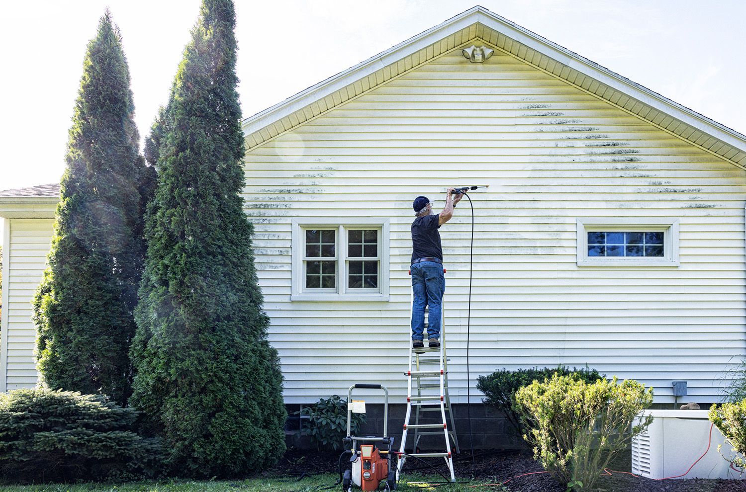 A man is standing on a ladder washing the side of a house.