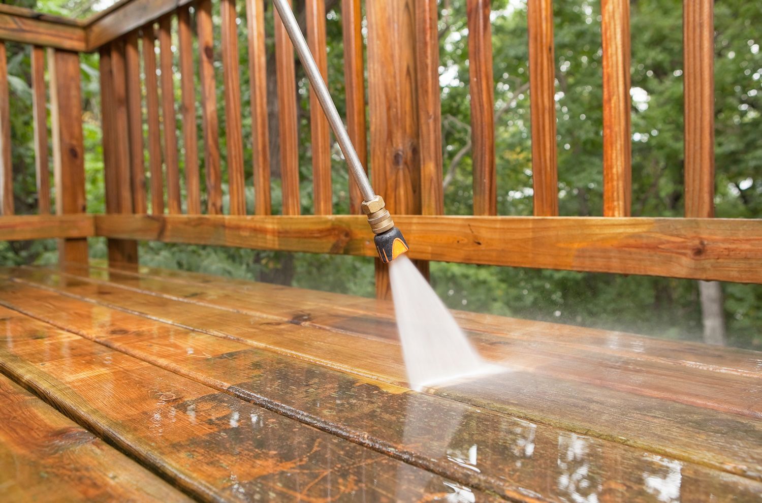 A person is using a high pressure washer to clean a wooden deck.