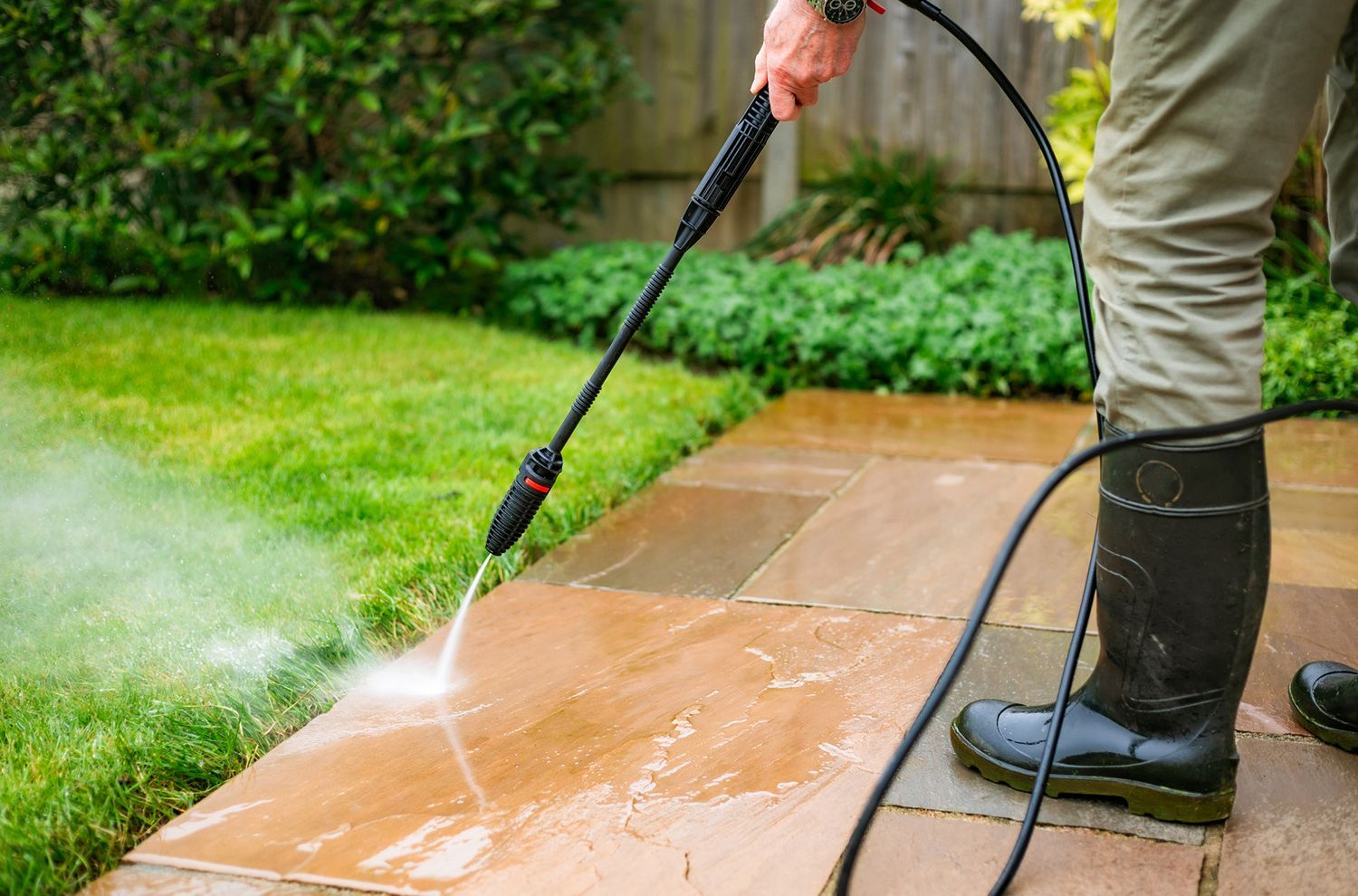 A man is using a high pressure washer to clean a patio.
