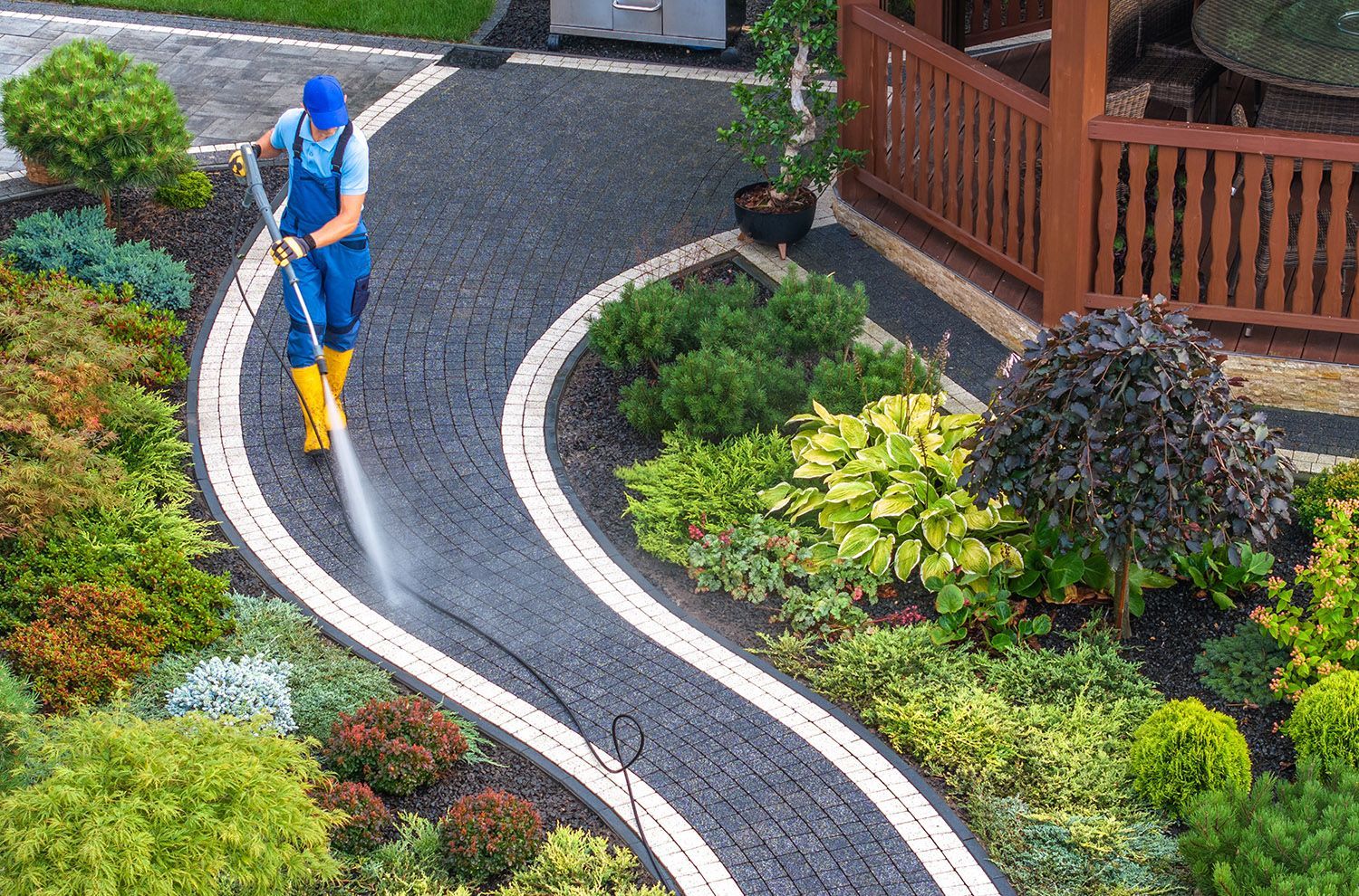 A man is using a high pressure washer to clean a walkway in a garden.