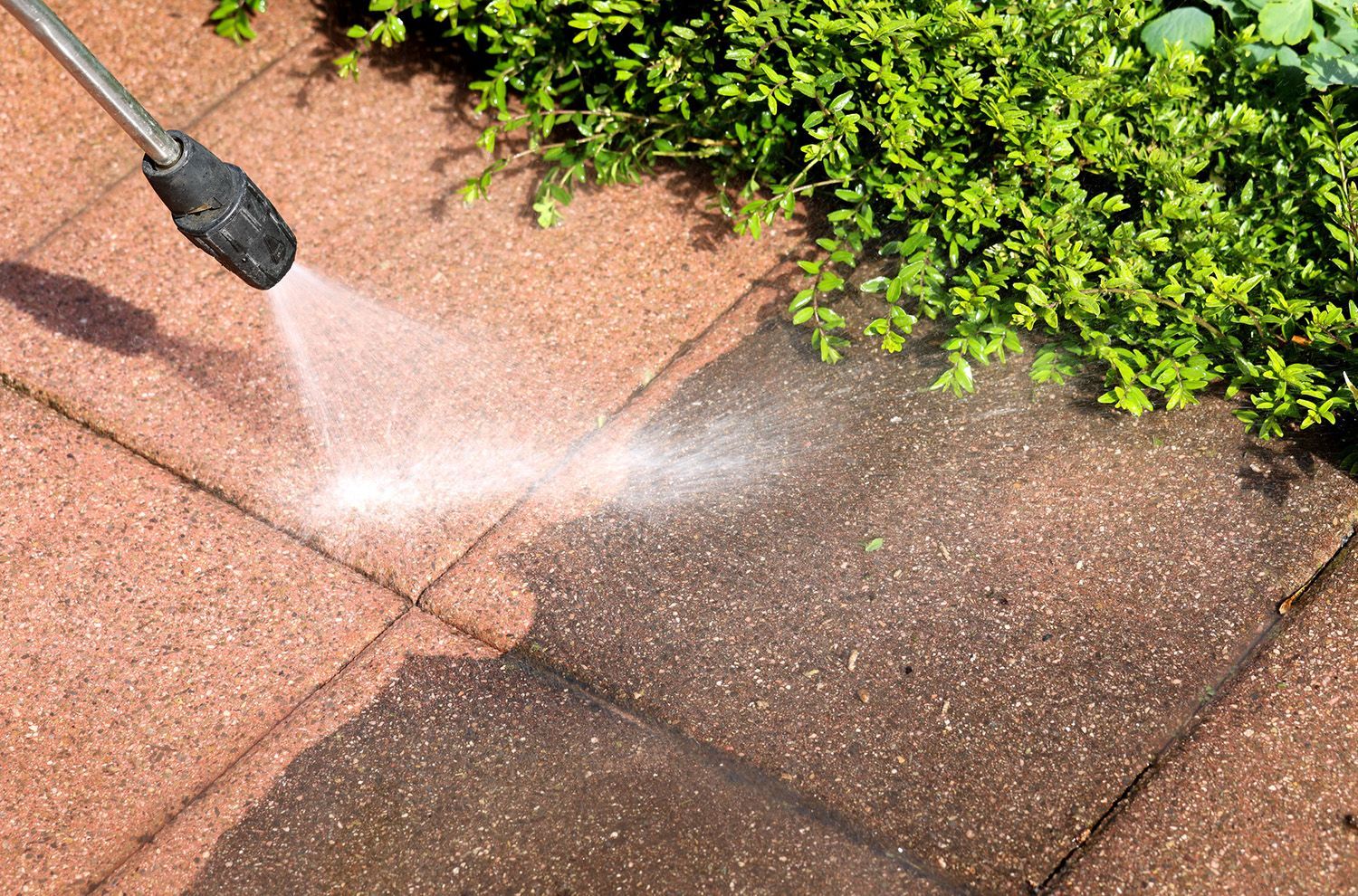 A person is using a high pressure washer to clean a brick walkway.