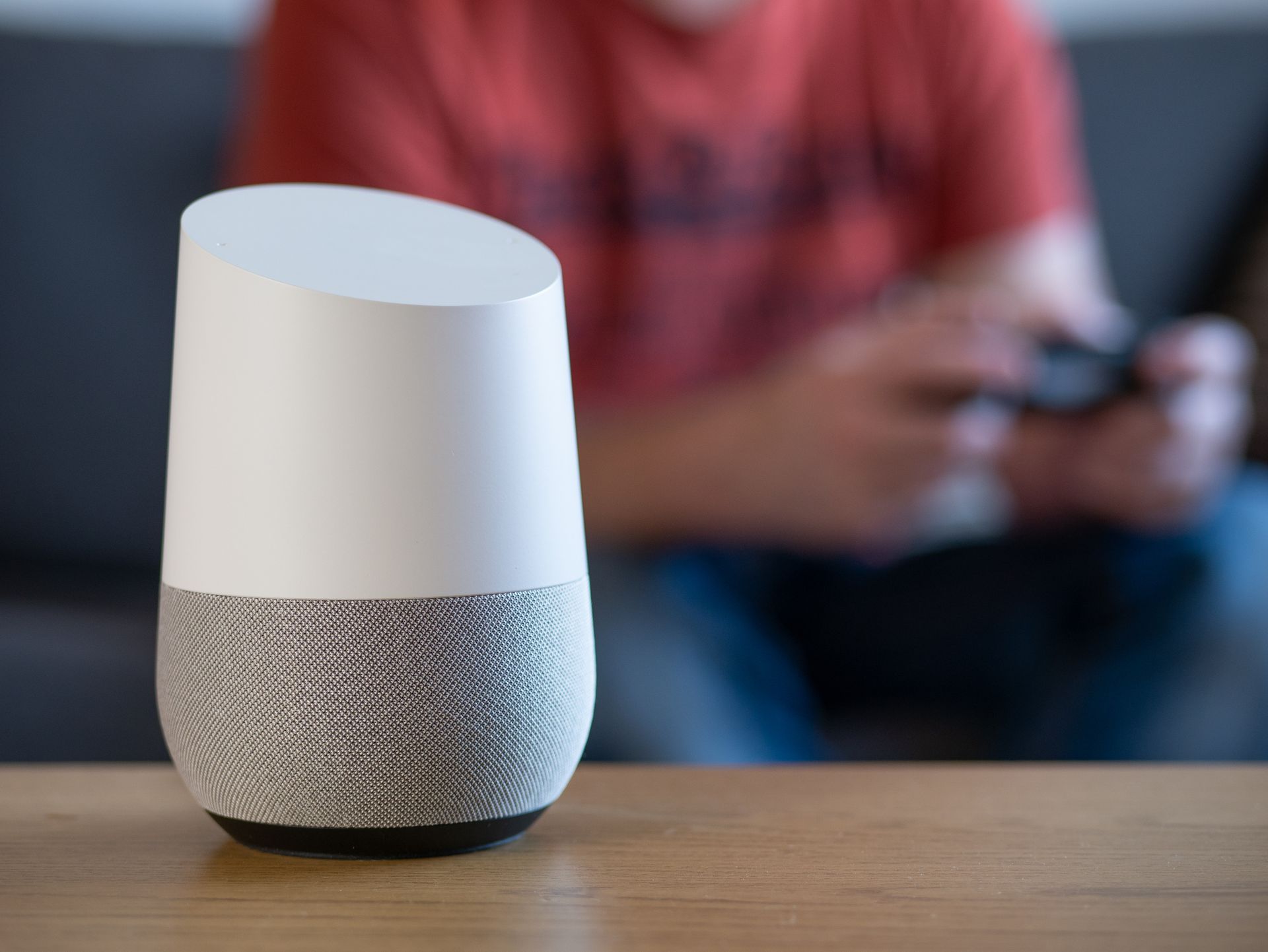 A smart speaker is sitting on a table next to a person playing a video game.