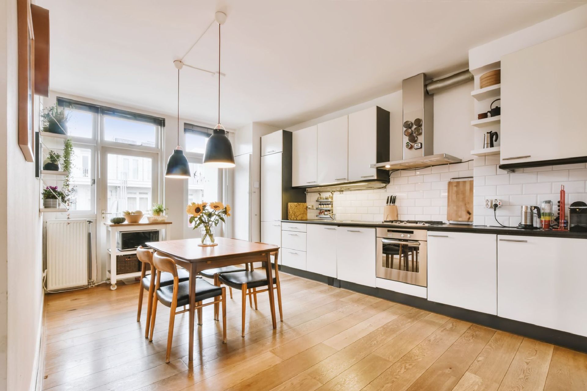 Une cuisine avec des armoires blanches, du parquet, une table et des chaises.