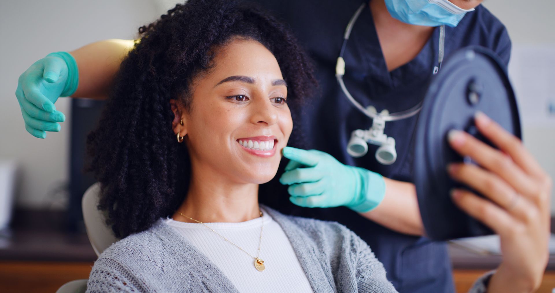 Smiling patient checks teeth in mirror as dentist examines them.
