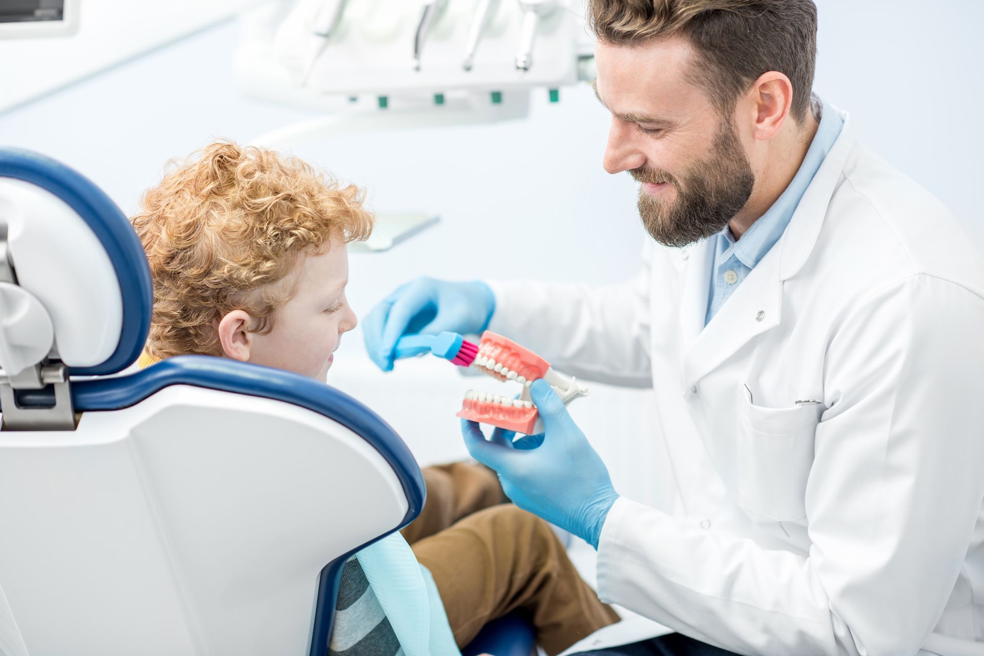 A pediatric dentist shows a boy how to brush teeth on an artificial jaw at Sacrey Dentistry & Associates in Geneva, IL