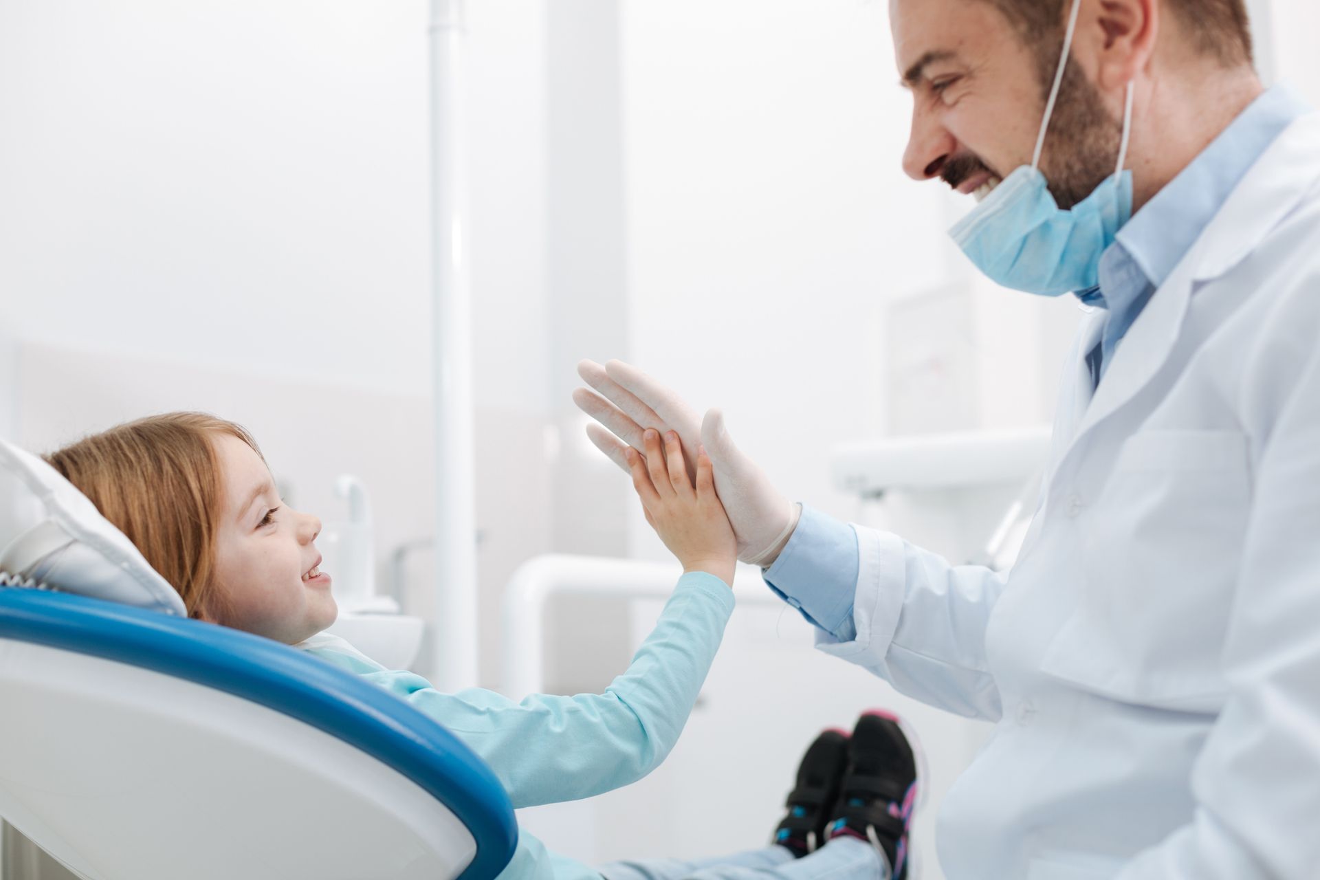 A pediatric dentist giving his little blonde patient a high-five at Sacrey Dentistry & Associates in Geneva, IL