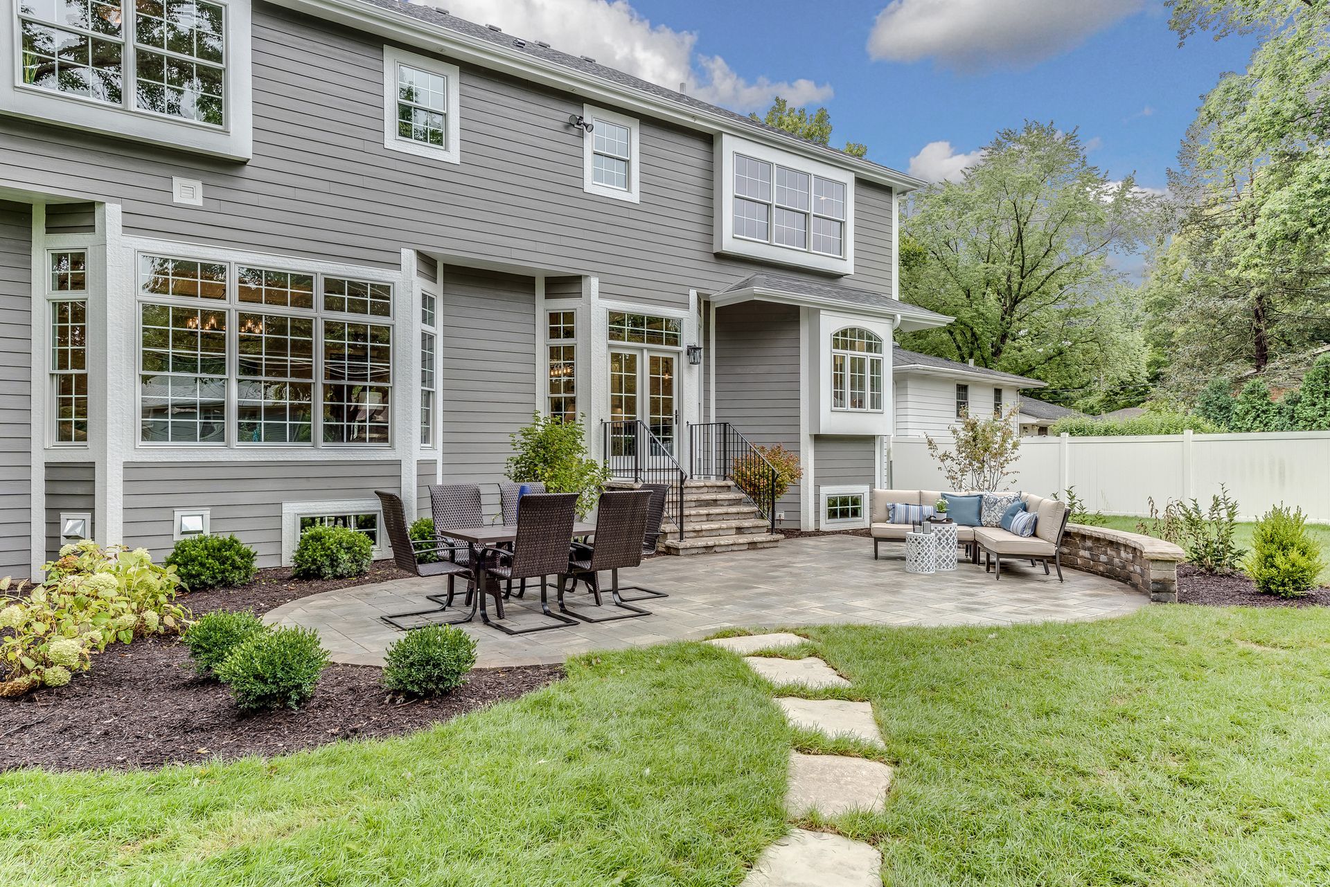 Spacious backyard patio building with seating, greenery, and a modern home exterior nearby. 