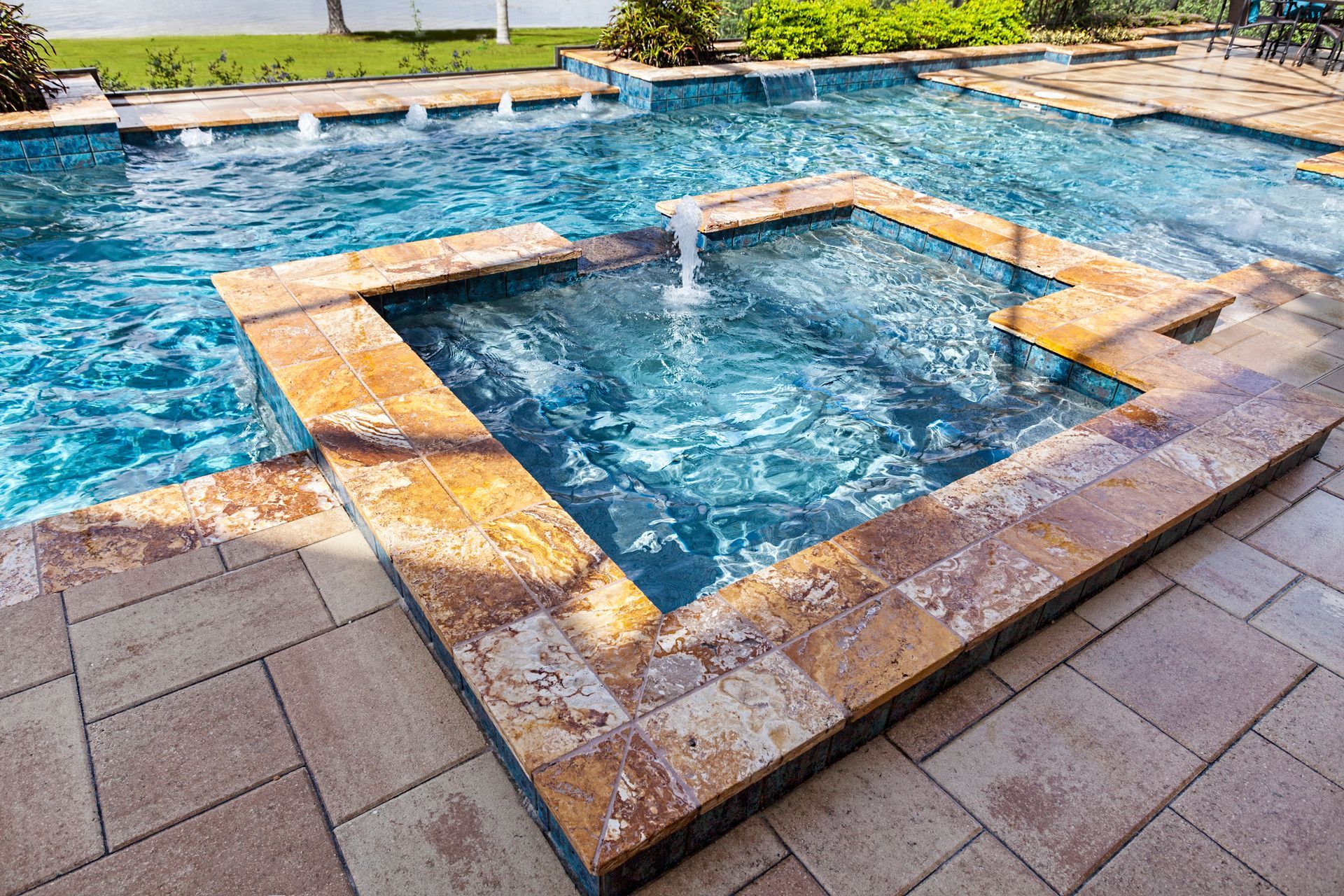 Luxury backyard pool with raised spa and flowing water features on stone tile patio surface design.