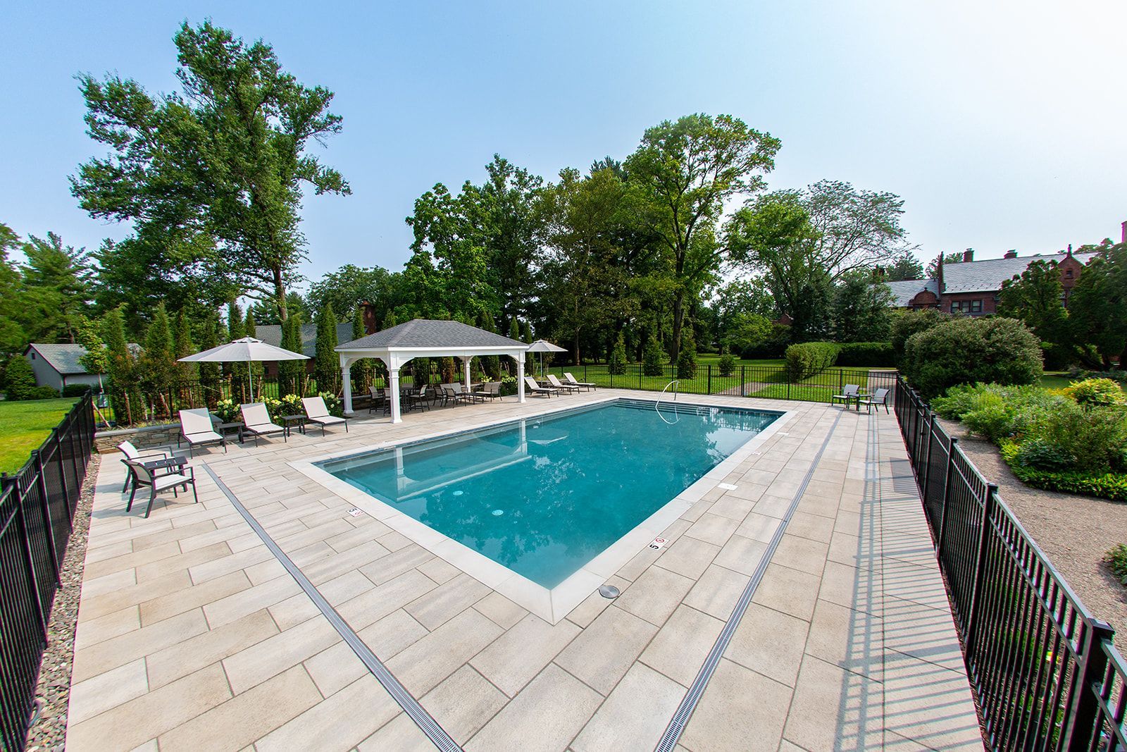Outdoor swimming pool with a white pergola and lounge chairs. Blue water and sunny sky.