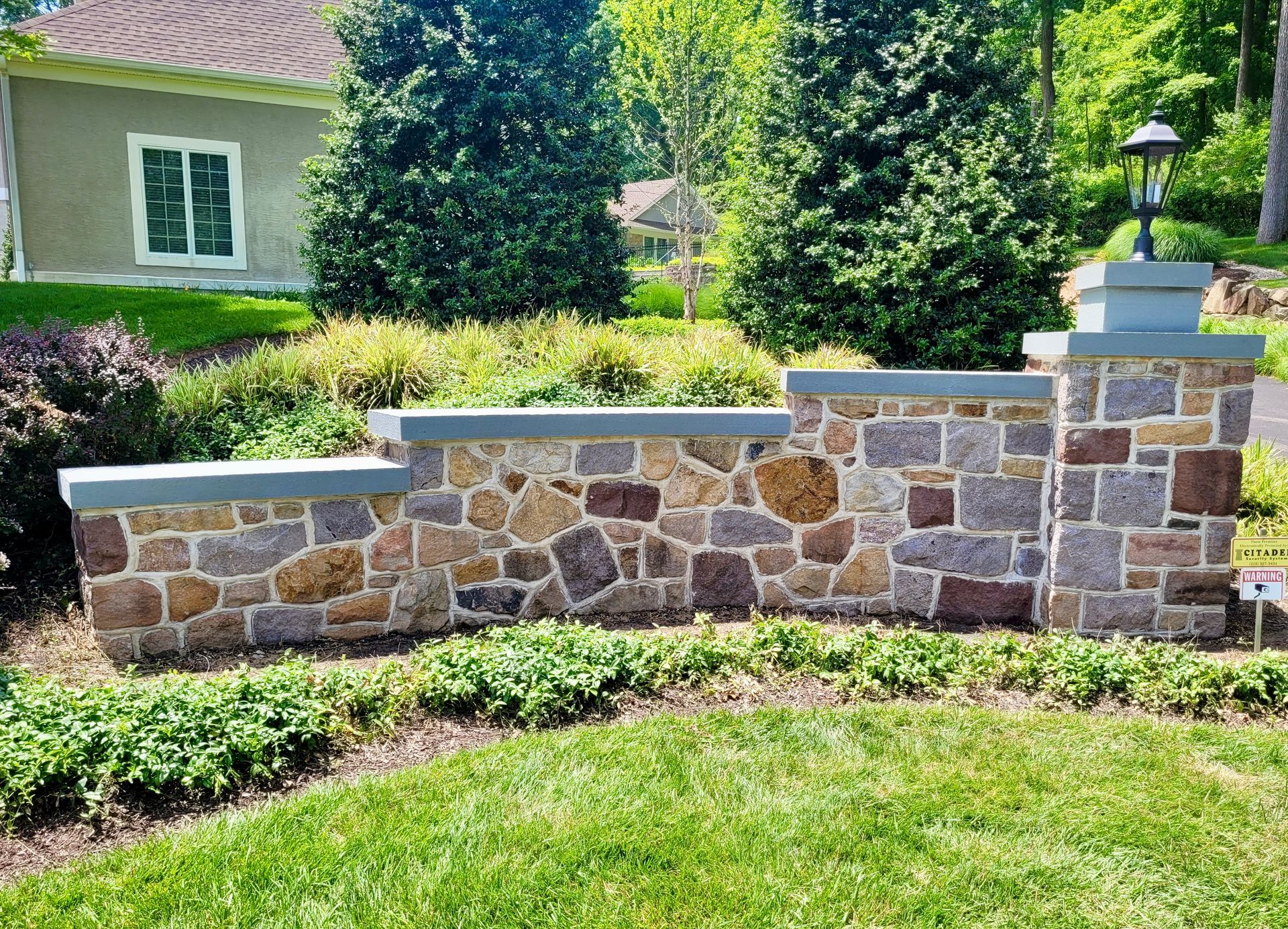 Stone retaining wall with gray caps, grass, and small house.