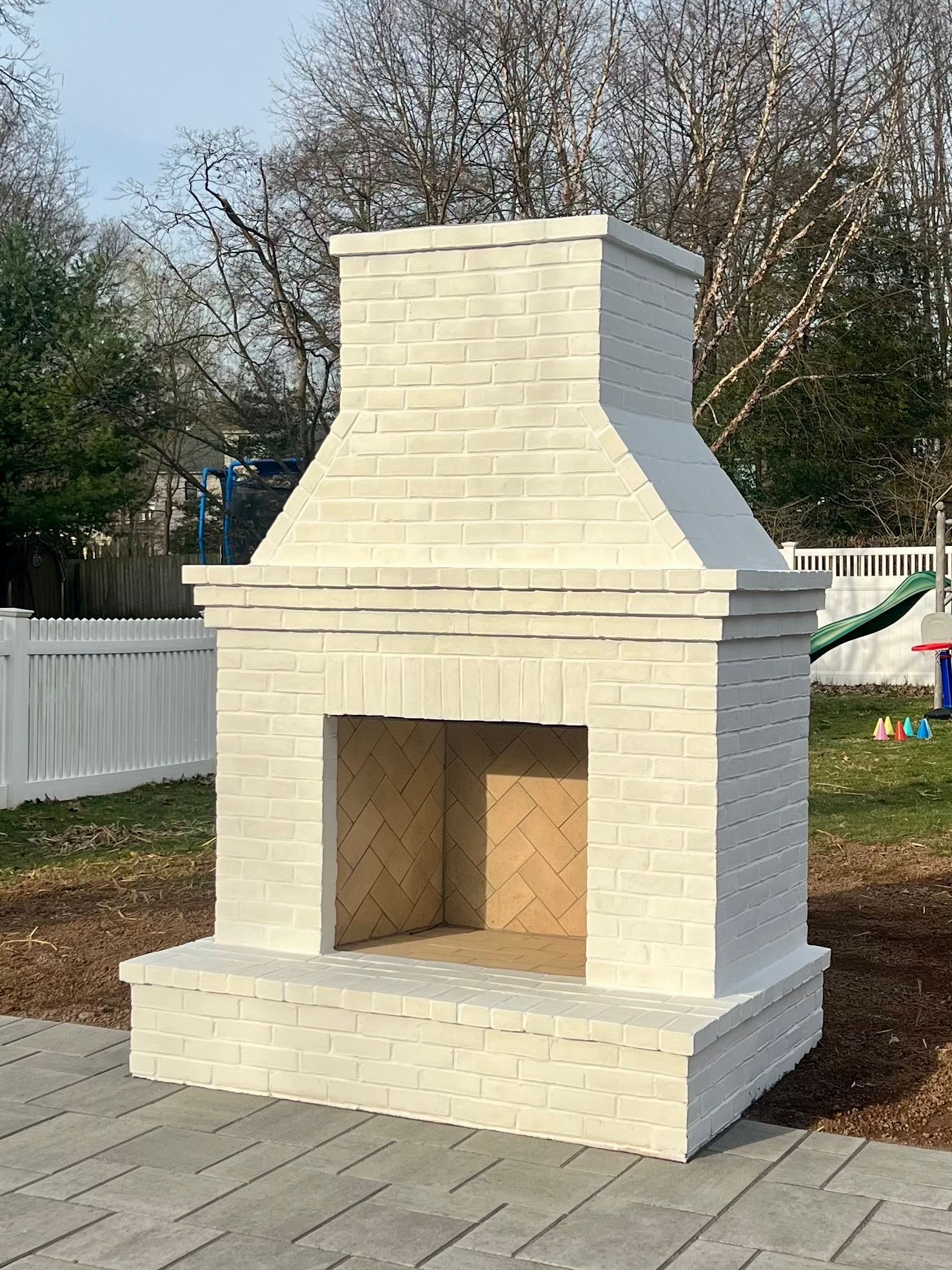 White brick outdoor fireplace on a brick patio in a yard.