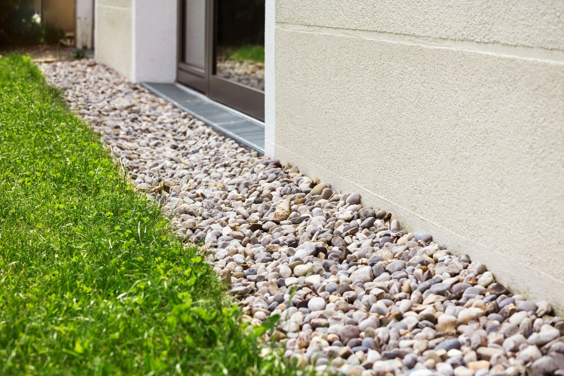 Pebble drainage next to a building with green grass on the side.