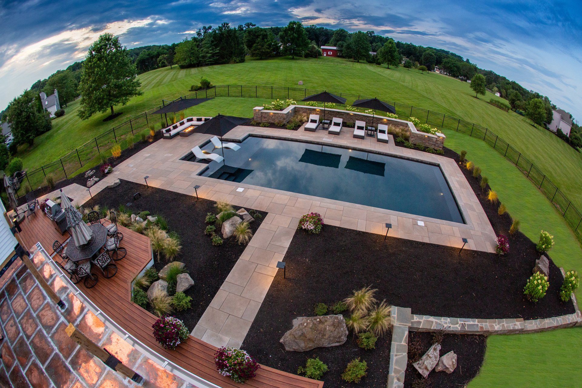 Luxury backyard pool with lounge chairs and landscaping, surrounded by fields.