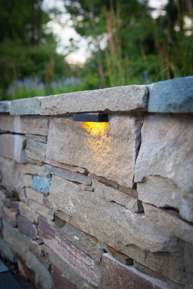 Stone retaining wall with built-in warm yellow LED light, in an outdoor setting.