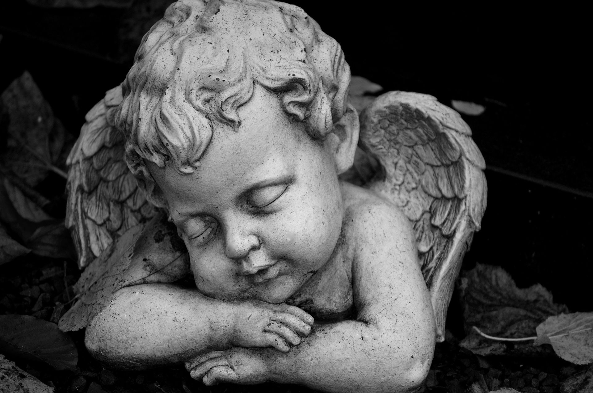 A black and white photo of a statue of a baby angel sleeping.